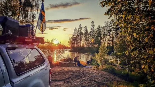 Lagerfeuer brennt am Ufer eines Sees, während ein Fahrzeug im Vordergrund steht