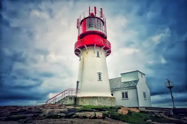 Leuchtturm mit rotem Oberteil und angrenzendem Gebäude auf felsigem Untergrund