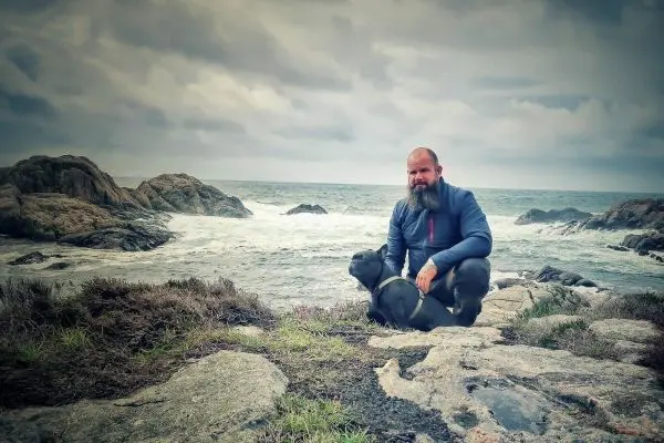 Mann sitzt auf Felsen am Meer mit Hund neben sich