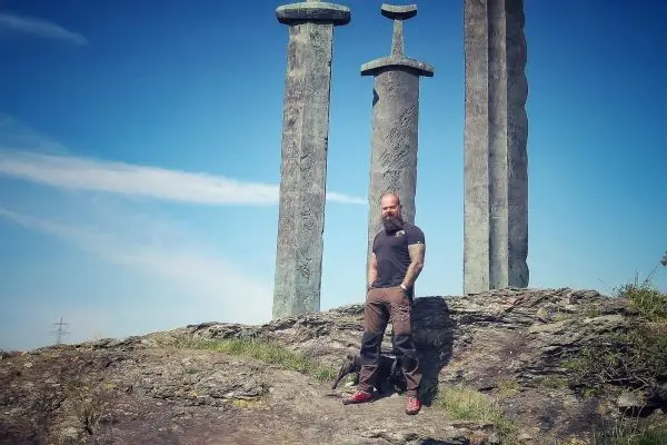 Mann steht auf Felsen vor drei großen, stilisierten Schwertern