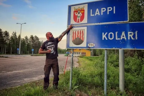 Mann zeigt auf Ortsschild mit den Namen Lappi und Kolari