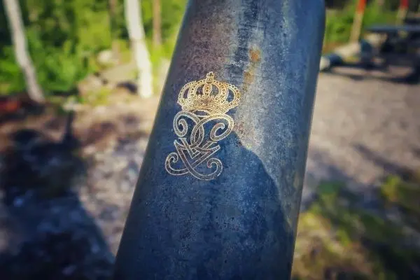 Metalloberfläche mit eingraviertem Wappen und Krone, umgeben von Natur