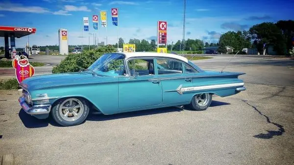 Oldtimer in blauer Lackierung parkt an einer Tankstelle mit Werbeschildern