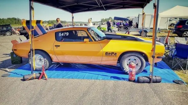 Orangefarbener Rennwagen steht unter einem Zelt auf einer blauen Plane