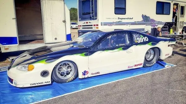 Rennwagen mit auffälligem Design steht auf einer blauen Plane neben einem Wohnmobil