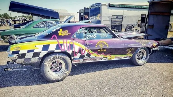 Rennwagen mit buntem Design steht auf einer Asphaltfläche neben einem Anhänger