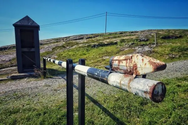 Rostige Schranke mit zwei Pfeilen auf einem Weg, im Hintergrund eine Holzhütte