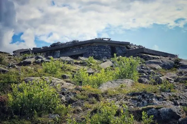 Ruine eines Steingebäudes auf einem bewachsenen Hügel mit Felsen und Pflanzen
