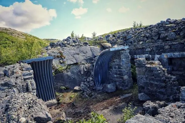 Ruinen mit Steinmauern und Metallteilen in einer bewachsenen Landschaft