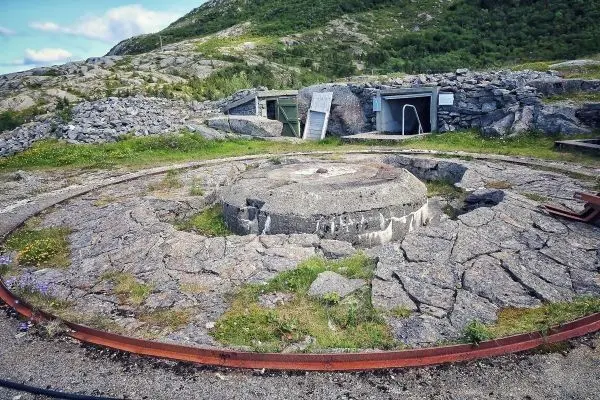 Runde Betonplattform mit rostigem Metallring und umgebenden Felsen in einer grünen Landschaft