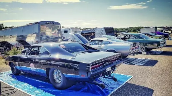 Schwarzer Muscle-Car steht auf einer blauen Plane, weitere Autos im Hintergrund