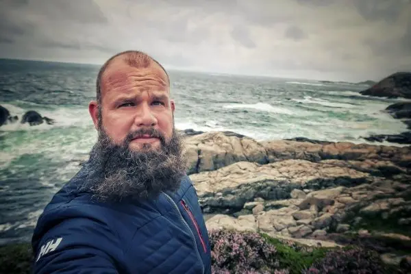Selbstporträt vor einer felsigen Küstenlandschaft mit Wellen und bewölktem Himmel
