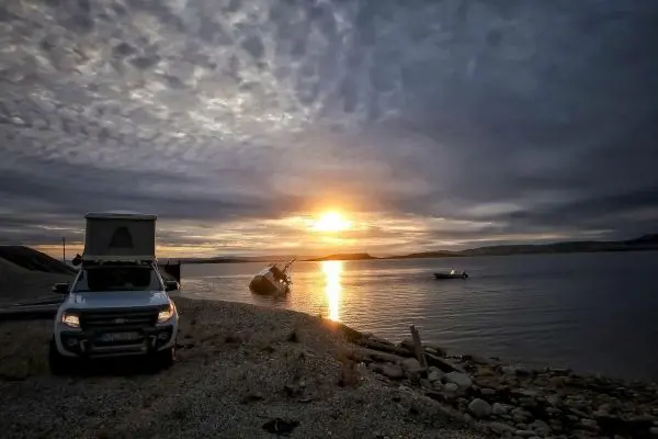Sonnenuntergang über einem Gewässer mit Fahrzeug und Boot am Ufer