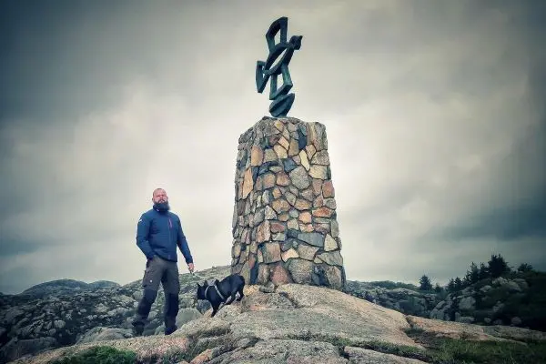 Steinmonument mit Skulptur, Mann steht neben Hund auf felsigem Untergrund