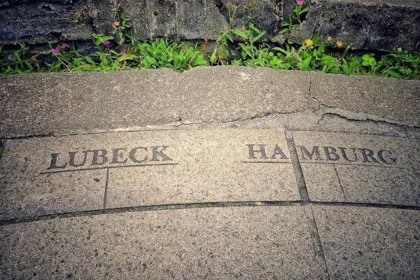 Steinplatte mit eingravierten Namen „Lübeck“ und „Hamburg“ auf grünem Untergrund