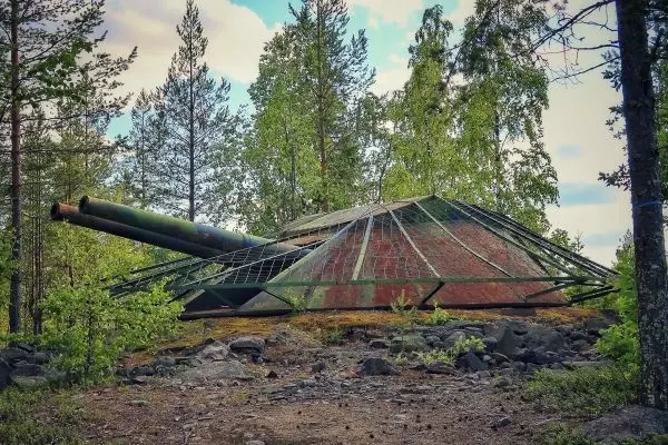 Verrostete Panzerkuppel mit zwei Kanonen, umgeben von Bäumen und Gestrüpp