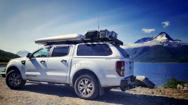 Weißer Geländewagen mit Dachgepäckträger steht am Ufer eines Sees