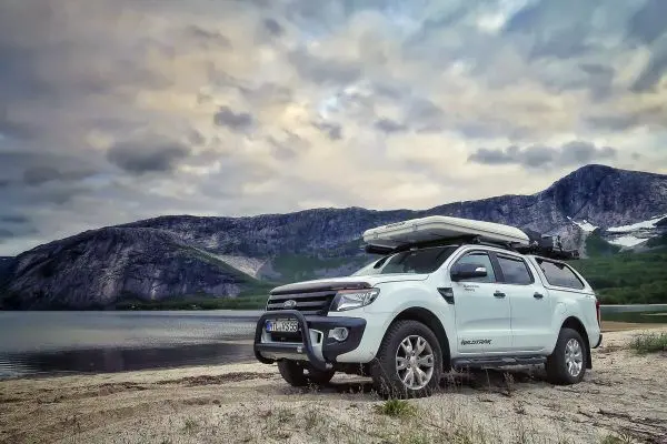Weißer Geländewagen steht am Ufer eines Sees vor einer Berglandschaft