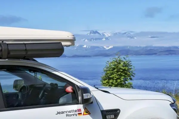 Weißes Fahrzeug mit Dachzelt vor einer Berglandschaft am Wasser