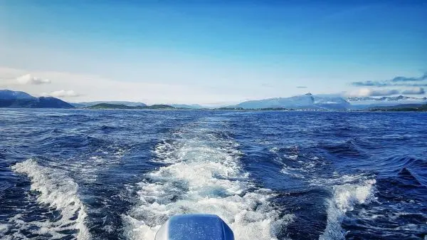 Wellen hinter einem Boot auf offenem Wasser mit Bergen im Hintergrund