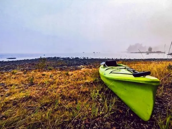 Grünes Kajak liegt am Ufer eines nebligen Gewässers zwischen Steinen und Gras