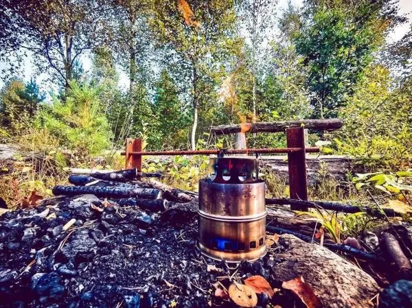 Hobo-Kocher mit Flamme auf schwarzem Bodenfeuer, Holzstücke daneben