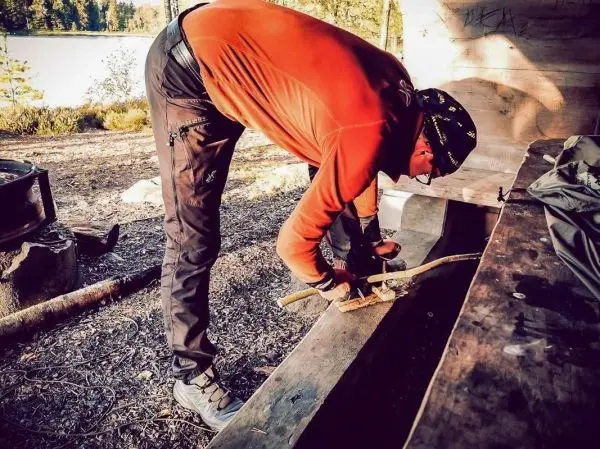Holzstück wird mit einem Messer bearbeitet, während eine Holzstruktur im Hintergrund sichtbar ist