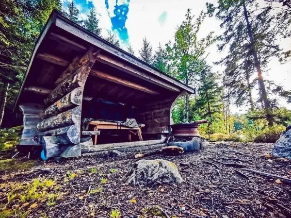 Hütte aus Holz steht im Wald mit einem Tisch und Stühlen