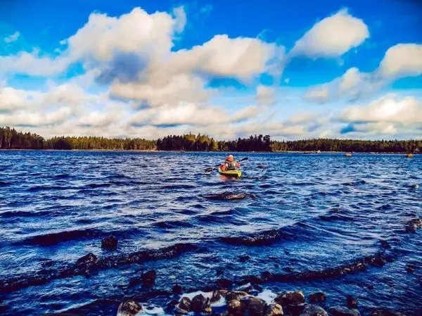 Kajakfahrer paddelt auf einem Gewässer mit Wellen und bewölktem Himmel