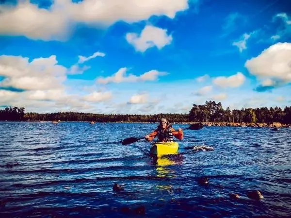 Kajakfahrer paddelt auf ruhigem Wasser unter blauem Himmel mit Wolken