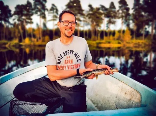 Mann hält gefangenen Fisch in einem Boot am Wasser