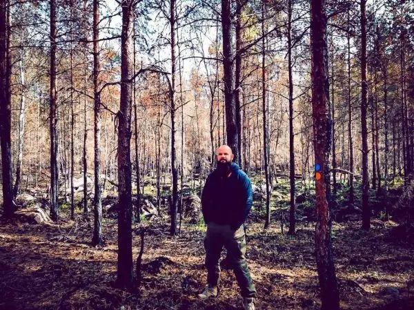 Mann steht zwischen Bäumen in einem Waldgebiet mit herbstlichen Farben