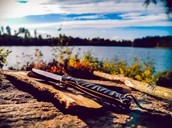 Messer liegt auf einem Holzstück am Ufer eines Sees, umgeben von Ästen