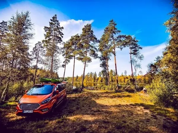 Oranger Van mit Kajak auf dem Dach steht in einer Waldlichtung