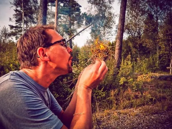 Person bläst auf ein Nest aus trockenem Gras beim Feuer machen