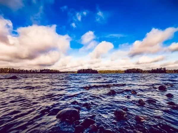 Wasserfläche mit Wellen und Steinen, bewölkter Himmel im Hintergrund