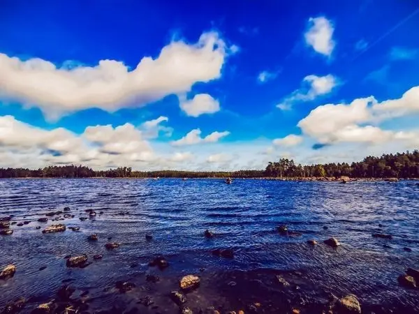 Wasserfläche mit Wellen und Steinen im Vordergrund, bewölkter Himmel im Hintergrund