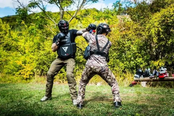 Zwei Kämpfer im Schutzanzug üben Schlagtechniken auf einer Wiese