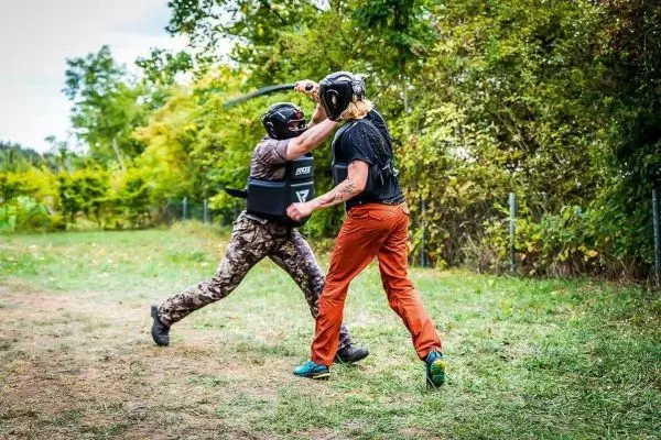 Zwei Personen in Schutzausrüstung führen einen Übungskampf mit einem Stock durch