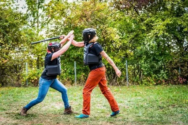 Zwei Personen in Schutzausrüstung führen einen Übungskampf mit einem Stock durch
