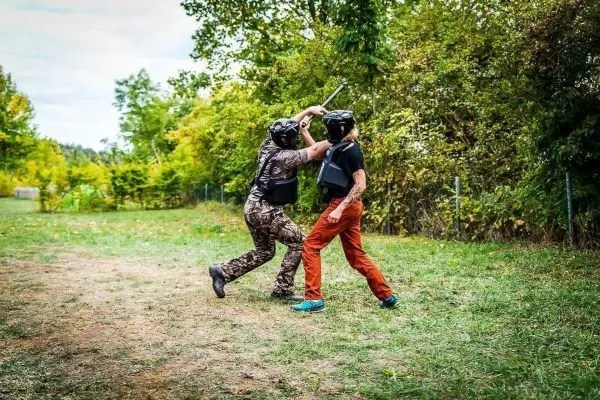 Zwei Personen in Schutzausrüstung führen einen Übungskampf mit Stöcken durch