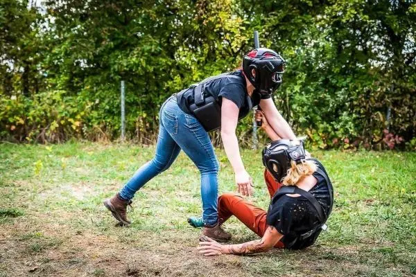 Zwei Personen in Schutzausrüstung üben Bodenkampf auf einer Wiese