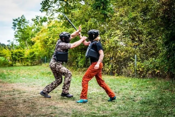 Zwei Personen in Schutzausrüstung üben einen Nahkampf mit einem Stock
