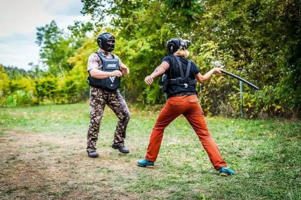 Zwei Personen in Schutzausrüstung üben mit einem Stock in einer Trainingssituation