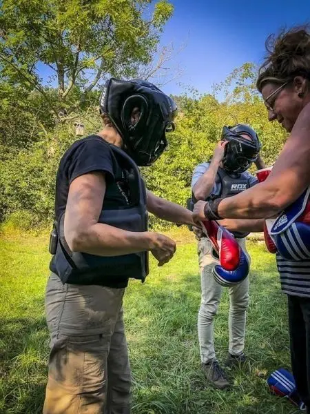 Drei Personen in Schutzausrüstung bereiten sich auf ein Boxtraining im Freien vor