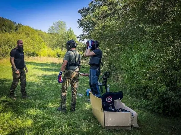 Drei Personen in Schutzausrüstung stehen auf einer Wiese, eine Person zieht einen Helm an