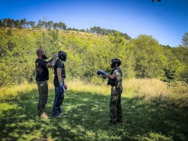 Drei Personen in Schutzausrüstung stehen auf einer Wiese, einer trägt Boxhandschuhe