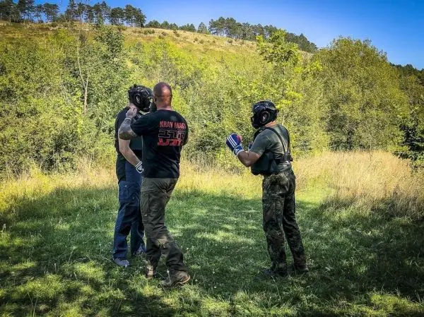 Drei Personen in Schutzausrüstung üben Techniken im Freien auf einer Wiese