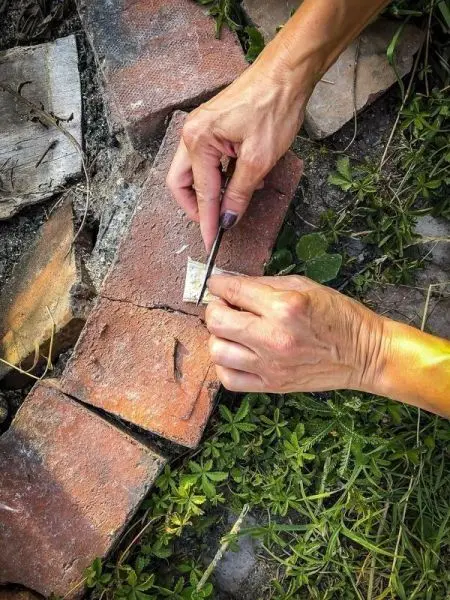 Hände nutzen einen kleinen Gegenstand, um auf einem Ziegelstein zu arbeiten