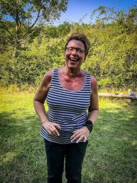 Lächelnde Person mit gestreiftem Oberteil steht auf einer Wiese